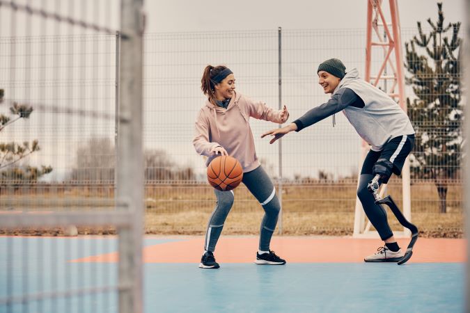 Happy athlete with artificial leg having fun while playing basketball with his girlfriend outdoors